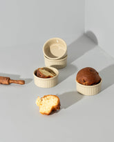 Three stoneware ramekins of varying sizes with lids, displayed on a neutral background. One ramekin contains a baked dessert, possibly a soufflé, and the other two are empty.